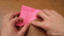 a close up of a person 's hands holding a piece of pink paper that says made in animatica on the bottom