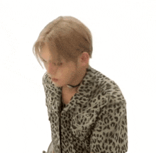 a young man in a leopard print shirt is sitting on a chair with his hands folded .