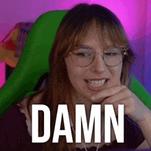 a woman wearing glasses and headphones is sitting in a green chair with the word damn written on her face