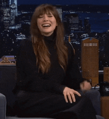 a woman wearing a black turtleneck is smiling in front of a city skyline