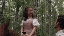 a girl in a pink dress stands next to a man on a horse in a forest