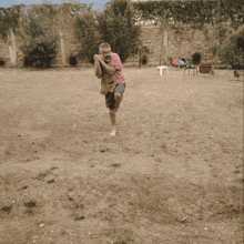 a man in a pink shirt stands on one leg in a field