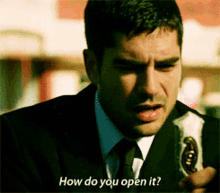 a man in a suit and tie is holding a bottle and asking how do you open it