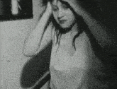 a black and white photo of a woman brushing her hair in a bathroom .
