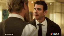 a man in a suit and tie talks to another man with #suitsla on the bottom