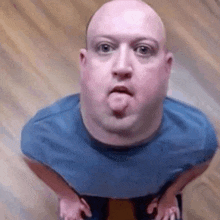 a bald man in a blue shirt is sticking his tongue out while looking up at the camera .