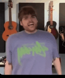 a man in a purple shirt is standing in front of a wall with guitars hanging on it .