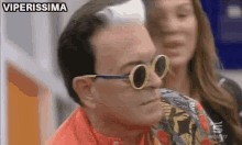 a man wearing sunglasses is sitting in front of a woman and a sign that says viperissima
