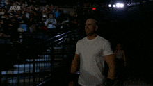 a man in a white shirt walks into a dark arena with a crowd behind him and a sign that says aew