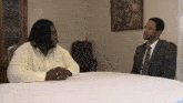 a man in a suit sits at a table with a man in a yellow shirt