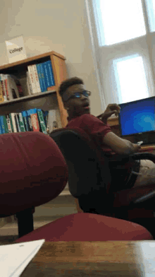 a man sits in front of a computer in front of a bookshelf that has a box that says college on it