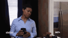 a woman in a blue shirt is holding a cup of coffee in front of a sistas logo