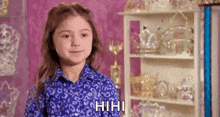 a little girl in a blue shirt is standing in front of a shelf of trophies .
