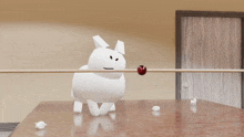 a white stuffed animal is laying on a table with a red ball in its mouth