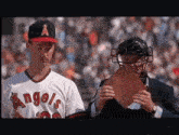 a baseball player wearing a angels jersey stands next to a catcher