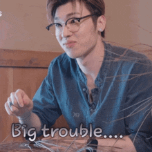a man wearing glasses is sitting at a table with the words " big trouble " on the bottom
