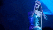 a woman with long pink hair is standing on a stage in a dark room .