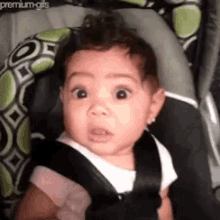 a baby is sitting in a car seat making a surprised face .