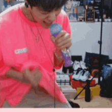 a man in a pink shirt is holding a microphone in his hand and singing into it .