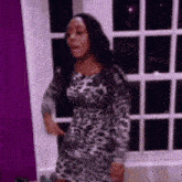 a woman in a leopard print dress is standing in front of a window .