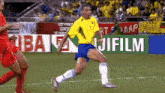 a soccer player in a yellow jersey is running on the field in front of fujifilm advertisements