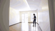 a woman is standing in an empty room with a white wall .