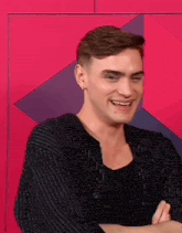 a man with his arms crossed is smiling in front of a pink background