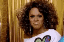 a woman with curly hair is wearing a white shirt with a butterfly on it and earrings .