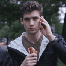a young man wearing a black jacket is holding a hot dog