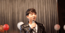 a young man in a leather jacket is holding a microphone in front of balloons .
