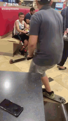 a boy with a prosthetic leg sits at a table in a restaurant while a man rides a skateboard