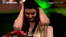 a woman is sitting at a table with her hands on her head and a watermark that says kinemaster