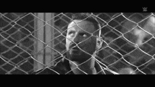 a black and white photo of a man behind a chain link fence with a w logo on the bottom