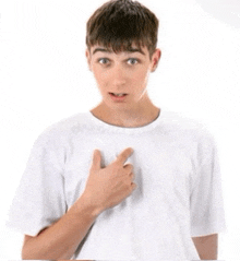 a young man in a white t-shirt is pointing at his chest