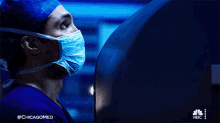 a man wearing a mask and a surgical cap is looking at a computer screen with #chicagomed written on the bottom