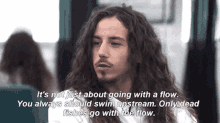 a man with long curly hair is talking about going with a flow