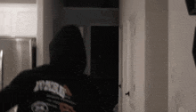 a man in a black hoodie is walking through a hallway .