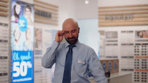 a man adjusts his glasses in front of a sign that says 50