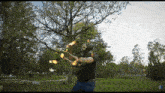 a man in a black shirt is juggling fire in a park with trees in the background