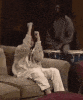 a man is playing drums while a woman sits on a couch with her arms in the air