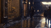 two men are walking down a wet sidewalk in front of a building that says ' a & a ' on it