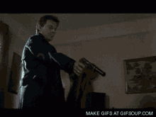 a man in a suit is holding a gun in a room with a gif soup.com watermark