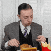 a man in a suit and tie eats a hamburger and french fries