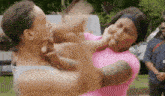 two women are fighting each other in a park while a man watches .