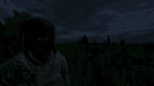 a person holding a gun in a dark field with trees in the background