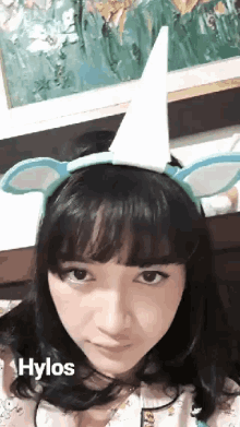 a girl wearing a headband with unicorn horns and ears says hylos on the bottom right