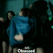 a woman in a blue jacket is dancing in a dark room with the words ms obsessed below her