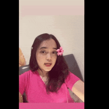 a woman in a pink shirt has a pink flower in her hair