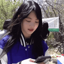 a girl in a blue jacket looks at her phone in front of a banner that says mt