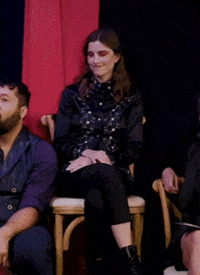 a man and a woman are sitting in chairs with a red curtain in the background